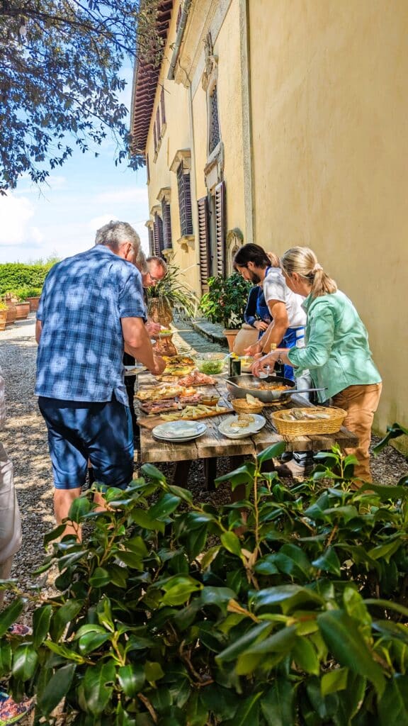 People surround table with lots of Tuscan food in sunny garden of Villa in Florence
