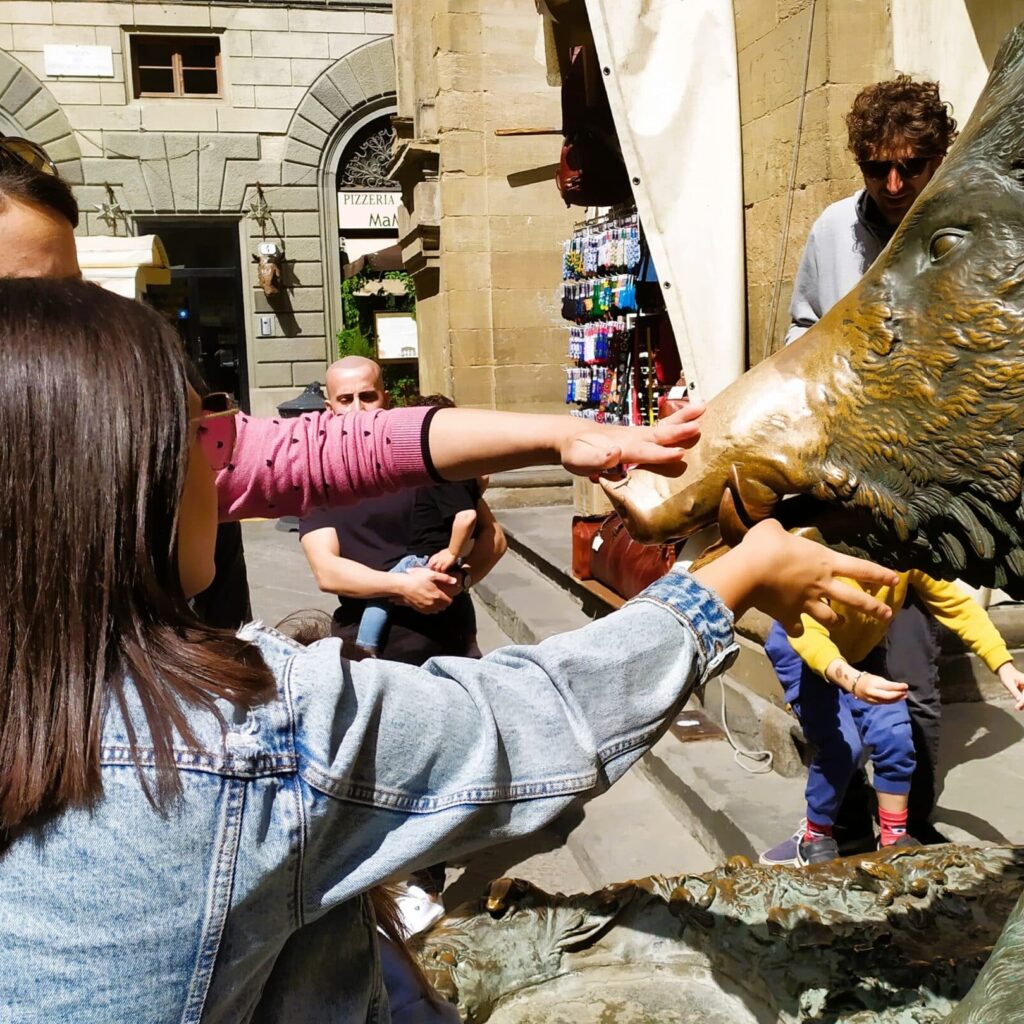 People touching the bronze statue of a wild boar, Il Porcellino, in Florence for good luck